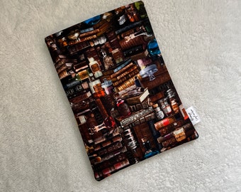 Puede incluir: Una bolsa de tela marrón con un estampado de libros y botellas vintage. La bolsa tiene una etiqueta blanca con el texto "shop small, shop local".