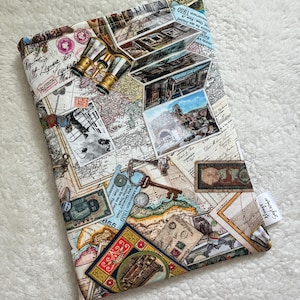 May include: A travel-themed book sleeve featuring a collage of vintage maps, stamps, and postcards. The sleeve is adorned with a pair of miniature gold and silver binoculars. The fabric has a cream background with a variety of colorful images.