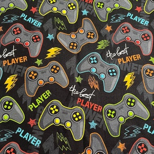 Op de afbeelding: Zwarte stof met een herhalend patroon van kleurrijke videogamecontrollers en de tekst "the best player".