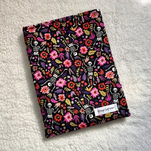 May include: Black fabric with a repeating pattern of pink, yellow, and white flowers and skeletons. The fabric has the text "Always September" printed on it.