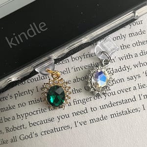 May include: Two book markers with clear plastic clips and decorative charms. One charm features a green gemstone surrounded by a gold setting with clear rhinestones. The other charm features a clear iridescent gemstone surrounded by a silver setting with clear rhinestones.