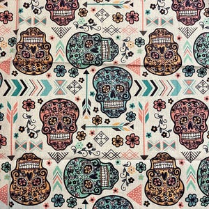 May include: A white fabric with a repeating pattern of colorful sugar skulls, flowers, and geometric shapes. The skulls are decorated with intricate details and have a whimsical, festive feel.