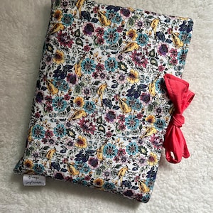 May include: A white pillow with a floral pattern featuring yellow birds and a pink bow. The pillow has a tag that says "Always September".