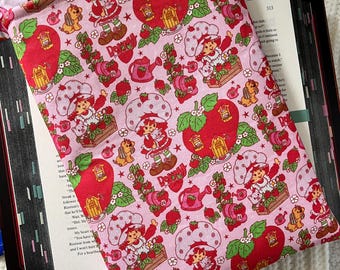 May include: Pink book sleeve with a repeating pattern of strawberries, houses, and a character named "Strawberry Shortcake". The sleeve has a white tag that says "Always September".