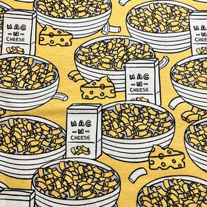 May include: A yellow background with a repeating pattern of bowls of macaroni and cheese, cheese wedges, and boxes that say "MAC -N- CHEESE".