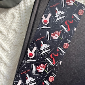 May include: A black bookmark with a repeating pattern of book covers from the Twilight series by Stephenie Meyer. The bookmark features the titles "Twilight", "Breaking Dawn", "New Moon", "Eclipse", and "Midnight Sun" in white and red against a black background.
