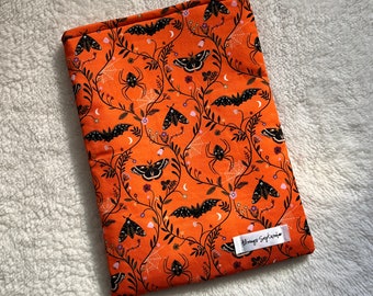 Peut inclure: Housse de livre en tissu orange avec un motif noir et blanc de papillons, d'araignées et de vignes. Le texte "Strange September" est imprimé sur la couverture.