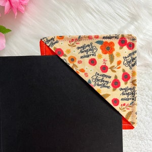 May include: A beige fabric bookmark with a red and orange floral pattern. The bookmark has the text "I'm a ray of fucking sunshine" printed on it.