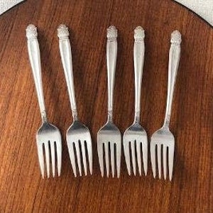 May include: Set of six silver forks with ornate handles. The forks are laid out on a wooden surface.