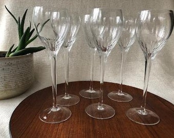 Puede incluir: Un juego de seis copas de vino de cristal transparente con tallos largos y delgados y un sutil patrón óptico en espiral grabado en la base de cada cuenco. Las copas presentan una forma redondeada y cónica con una base circular plana y ancha.