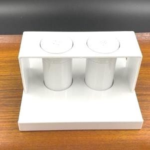 May include: White ceramic salt and pepper shakers in a white ceramic holder. The shakers have a round top and a cylindrical body.