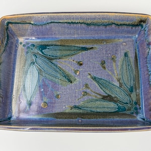 May include: Rectangular ceramic serving tray with a blue and purple glaze. The tray features a floral design in shades of green and blue. It has twisted rope handles with floral accents on each end.