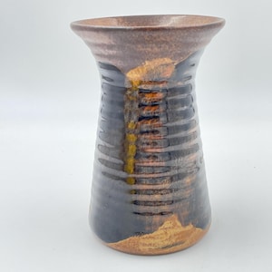 May include: A handcrafted ceramic vase with a flared rim and a textured, ribbed body. The vase has a brown, black, and gold colour scheme, with a glossy finish. This vase is a decorative item for the home.