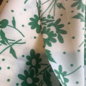 May include: White fabric with a green floral pattern. The fabric has a subtle texture and the flowers are a simple, stylized design.