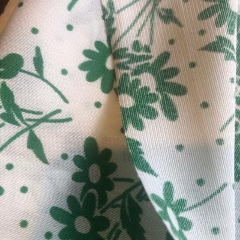 May include: White fabric with a green floral pattern. The fabric has a subtle texture and the flowers are a simple, stylized design.