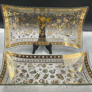 Könnte beinhalten: Zwei transparente Glasservierplatten mit Blattgold-Designs. Die Platten sind rechteckig mit abgerundeten Ecken und weisen ein Blumenmuster mit goldenen Akzenten auf.