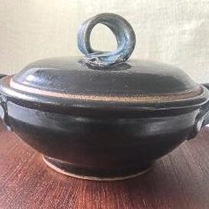 May include: A black ceramic serving dish with a lid. The dish has two handles on the sides and a single handle on the lid. The lid has a blue-green glaze.