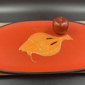 May include: A red oval serving tray with a black rim and a white outline of a fish. The tray has two handles on the sides. The text "Niagara Falls Canada" is printed on the tray.
