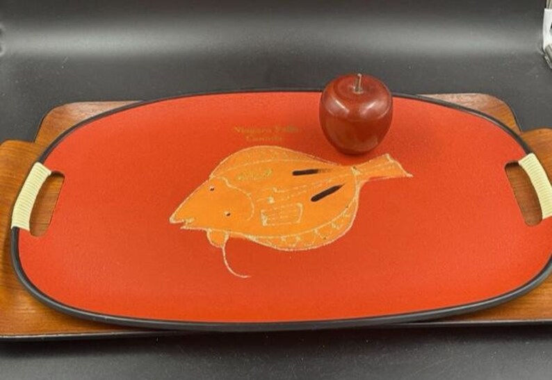 May include: A red oval serving tray with a black rim and a white outline of a fish. The tray has two handles on the sides. The text "Niagara Falls Canada" is printed on the tray.