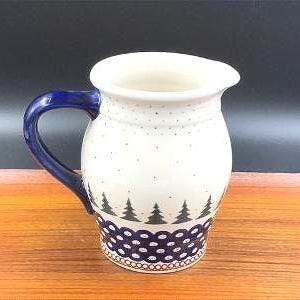 Könnte beinhalten: Eine weiße Keramikkanne mit blauem Henkel und einem grün-blauen Muster aus Bäumen und Punkten.