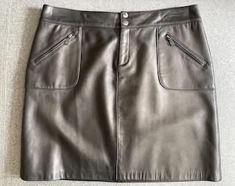 May include: A black leather skirt with two front pockets and two zipped pockets. The skirt has a button and zip closure. The skirt is made of a smooth, matte leather material.
