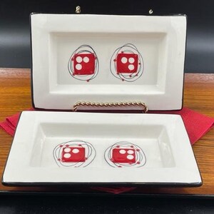 May include: Two white ceramic rectangular dishes with black trim. Each dish features a red dice with white dots inside a black circle design.