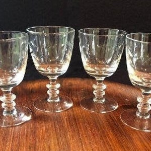 May include: Four clear wine glasses with a textured bowl design and a decorative stem. The glasses are displayed on a wooden surface, highlighting their elegant shape and clarity. Ideal for serving wine or other drinks.
