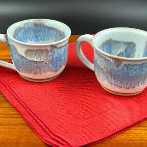 May include: Two ceramic mugs with a blue and white glaze pattern. The mugs have a rounded shape and a handle on the side.
