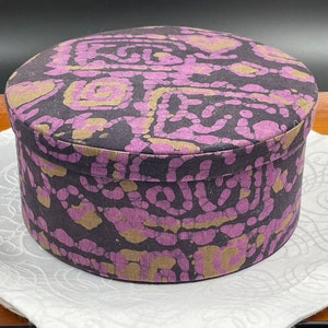 May include: A round, purple and gold fabric storage box with a batik pattern.