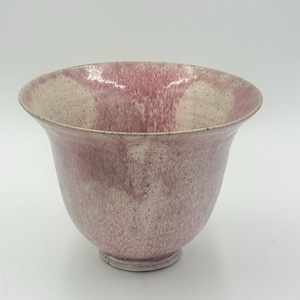 Könnte beinhalten: Eine handgefertigte Keramikschale mit ausgestelltem Rand und einer gesprenkelten, strukturierten Oberfläche. Die Schale hat einen Farbverlauf aus Rosa- und Off-White-Tönen, der ein einzigartiges Aussehen erzeugt. Die Schale hat einen kleinen, kreisförmigen Boden.