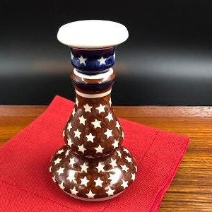 May include: A brown ceramic candle holder with a white top and blue accents. The holder is decorated with white stars on a brown background.