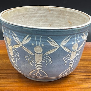 May include: A blue ceramic bowl with a white glaze and a design of white lobsters around the rim.