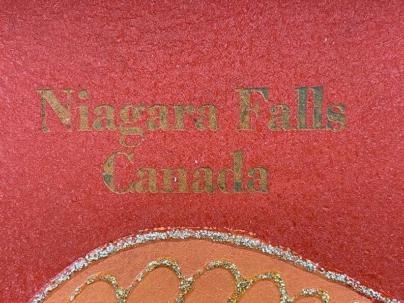 May include: A red background with gold lettering that reads "Niagara Falls Canada".