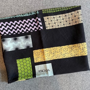 May include: Black silk scarf with a geometric pattern in shades of green, yellow, and blue. The scarf features the word "ESCADA" in white lettering.