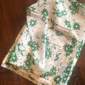 May include: White fabric with a green floral pattern. The fabric is folded in half and the pattern is visible on both sides.