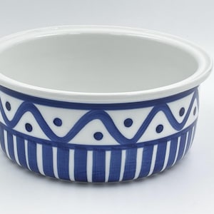 May include: White ceramic bowl with a blue and white decorative pattern. The bowl features a blue wave and dot design, with vertical blue stripes at the base. The interior is plain white.