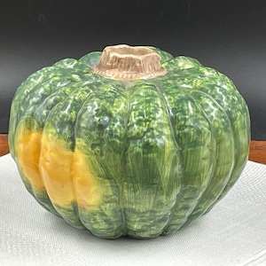 May include: A ceramic pumpkin vase with a green and yellow glaze. The vase has a textured surface that resembles the skin of a pumpkin.
