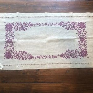 Puede incluir: Un camino de mesa de lino blanco con un borde bordado de flores moradas.