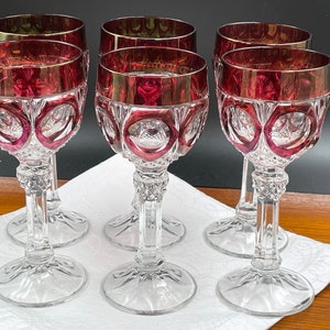 May include: Set of six clear glass wine glasses with a burgundy colored rim and intricate cut glass design.