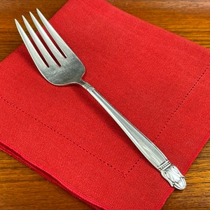 May include: A silver fork with a decorative handle rests on a red cloth napkin.