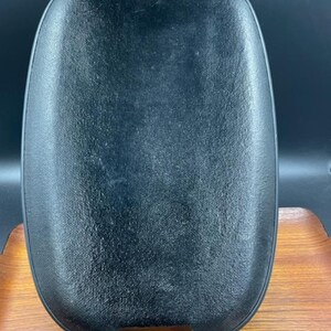May include: A black oval serving tray with woven rope handles. The tray has a textured surface.