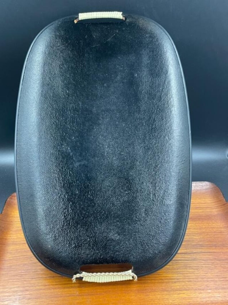 May include: A black oval serving tray with woven rope handles. The tray has a textured surface.
