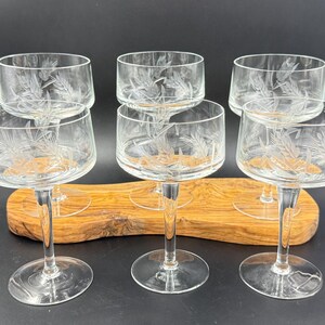 May include: Six clear champagne glasses with etched wheat or leaf designs. The glasses are arranged on a wooden serving tray. Each glass has a round bowl and a long, slender stem.
