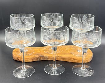 Op de afbeelding: Zes heldere champagneglazen met geëtste tarwe- of bladmotieven. De glazen zijn gerangschikt op een houten serveerblad. Elk glas heeft een ronde kom en een lange, slanke steel.