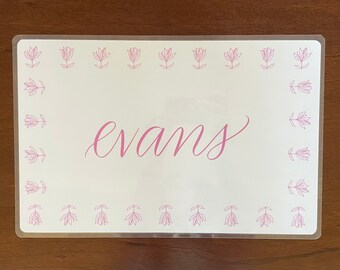 May include: White placemat with a pink floral border and the name "Evans" written in pink cursive.