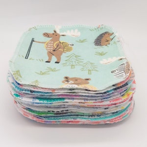 May include: A stack of 20 reusable cotton rounds with a woodland animal print. The top round features a light blue background with a deer, hedgehog, and trees. The rounds are sewn with a white zig-zag stitch.