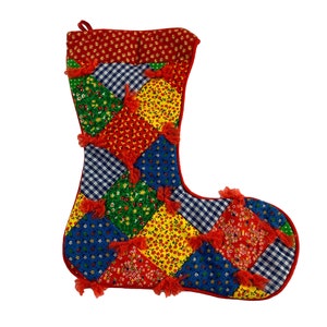 May include: A red Christmas stocking with a patchwork design. The stocking is made of different colored fabrics with floral patterns and gingham. The stocking has red tassels around the edges.