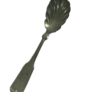 May include: A silver sugar spoon with a shell-shaped bowl and a detailed handle.