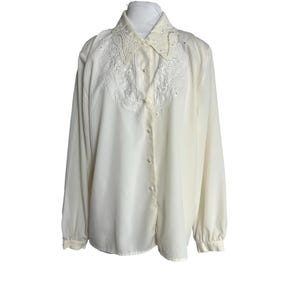 May include: A white long-sleeved button-up blouse with a lace collar and cuffs. The blouse has a pearl-like button closure.