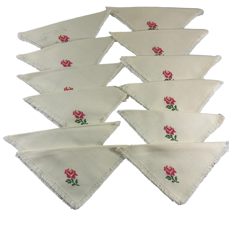 May include: Set of twelve white linen napkins with a red rose embroidered in the center of each napkin. The napkins have a fringed edge.